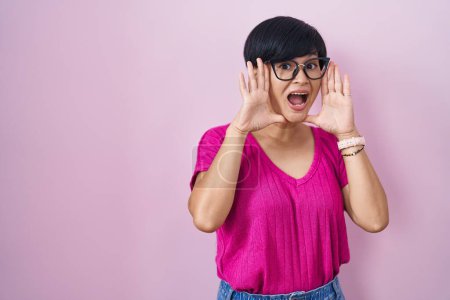 Téléchargez les photos : Jeune femme asiatique avec les cheveux courts debout sur fond rose souriant joyeux jeu jeter un coup d'oeil avec les mains montrant le visage. surpris et sortis - en image libre de droit
