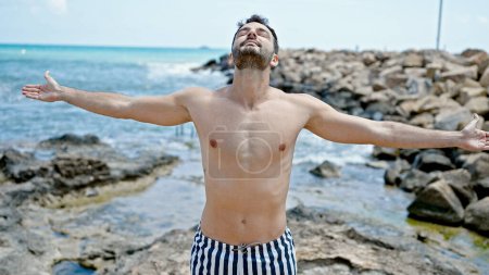 Foto de Joven turista hispano con traje de baño respirando con los brazos abiertos en la playa - Imagen libre de derechos