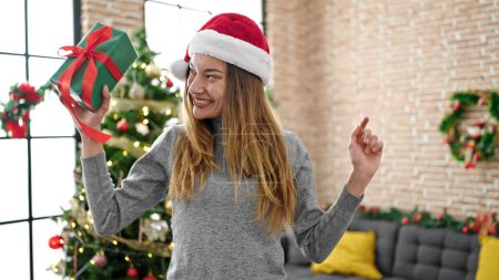 Téléchargez les photos : Jeune femme caucasienne tenant cadeau de Noël dansant à la maison - en image libre de droit