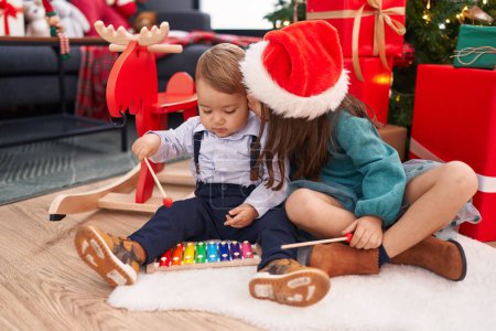 Photo for Adorable boy and girl playing xylophone celebrating christmas kissing at home - Royalty Free Image