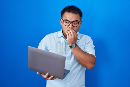 Photo for Chinese young man using computer laptop looking stressed and nervous with hands on mouth biting nails. anxiety problem. - Royalty Free Image