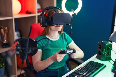 Téléchargez les photos : Jeune rousse femme streamer jouer jeu vidéo en utilisant des lunettes de réalité virtuelle et joystick à la salle de jeu - en image libre de droit