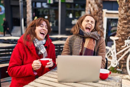 Téléchargez les photos : Two women mother and daughter using laptop drinking coffee at coffee shop terrace - en image libre de droit