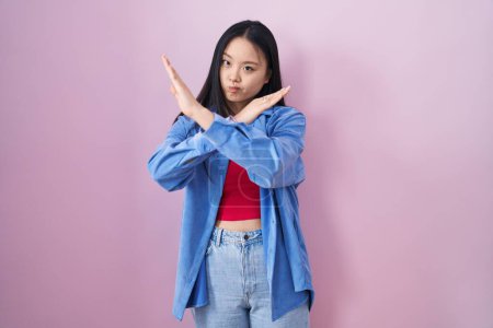 Photo for Young asian woman standing over pink background rejection expression crossing arms doing negative sign, angry face - Royalty Free Image