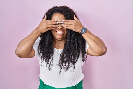 Photo for Plus size hispanic woman standing over pink background covering eyes with hands smiling cheerful and funny. blind concept. - Royalty Free Image