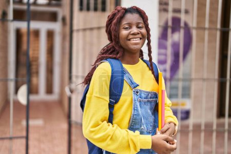 Foto de Estudiante afroamericana sonriendo confiada sosteniendo libros en la universidad - Imagen libre de derechos