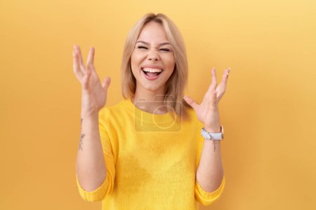 Photo for Young caucasian woman wearing yellow sweater crazy and mad shouting and yelling with aggressive expression and arms raised. frustration concept. - Royalty Free Image