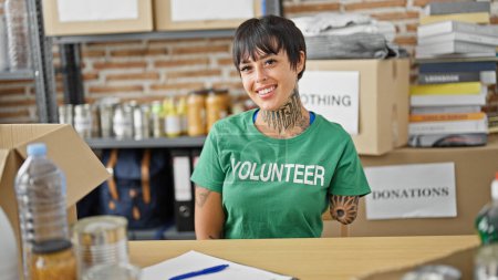 Photo for Hispanic woman with amputee arm volunteer smiling confident sitting on table at charity center - Royalty Free Image