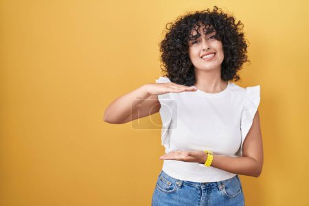 Photo for Young middle east woman standing over yellow background gesturing with hands showing big and large size sign, measure symbol. smiling looking at the camera. measuring concept. - Royalty Free Image