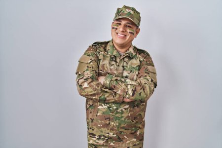 Téléchargez les photos : Jeune homme hispanique portant uniforme de camouflage visage heureux de l'armée souriant avec les bras croisés regardant la caméra. personne positive. - en image libre de droit