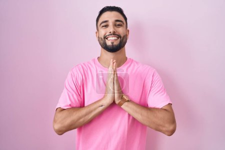 Photo for Hispanic young man standing over pink background praying with hands together asking for forgiveness smiling confident. - Royalty Free Image