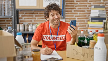 Photo for Young hispanic man volunteer writing on clipboard having video call at charity center - Royalty Free Image