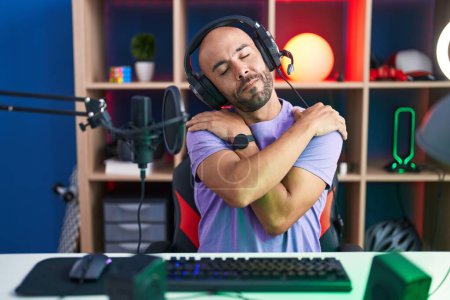 Photo for Middle age bald man playing video games wearing headphones hugging oneself happy and positive, smiling confident. self love and self care - Royalty Free Image