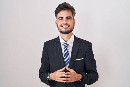 Photo for Young hispanic man with tattoos wearing business suit and tie hands together and fingers crossed smiling relaxed and cheerful. success and optimistic - Royalty Free Image