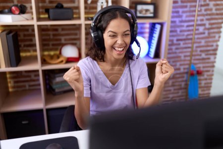 Photo for Young african american woman streamer playing video game with winner expression at gaming room - Royalty Free Image