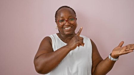 Photo for Joyful african american woman standing confidently, happily pointing and presenting over isolated pink background. adults expression of positive joy, showing copy space with fingers. - Royalty Free Image