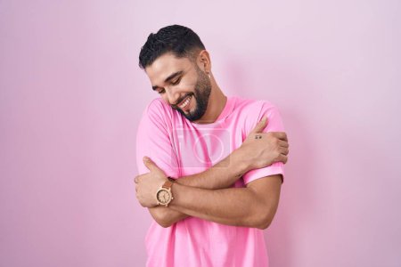 Téléchargez les photos : Jeune homme hispanique debout sur fond rose se serrant dans ses bras heureux et positifs, souriant confiant. amour de soi et soins de soi - en image libre de droit
