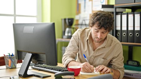 Foto de Joven trabajador de negocios hispano usando computadora tomando notas en la oficina - Imagen libre de derechos
