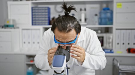 Photo for Focused young chinese man, a dedicated scientist at the heart of medical technology, deeply immersed in biology research using microscope in lab. - Royalty Free Image