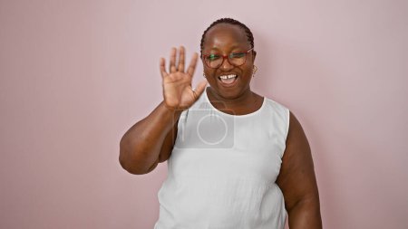 Téléchargez les photos : Femme afro-américaine confiante disant joyeusement bonjour, souriant sur fond rose isolé, vague de main exprimant des vibrations positives - en image libre de droit