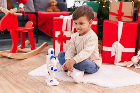 Photo for Adorable hispanic boy playing with robot toy sitting on floor by christmas tree at home - Royalty Free Image