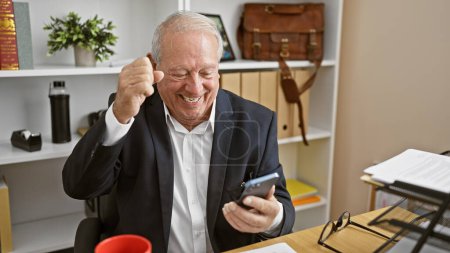 Téléchargez les photos : Senior homme d'affaires en utilisant smartphone célébrant au bureau - en image libre de droit