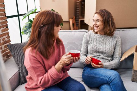 Photo for Two women mother and daughter drinking coffee sitting on sofa at new home - Royalty Free Image