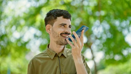 Photo for Young hispanic man sending voice message with smartphone at park - Royalty Free Image