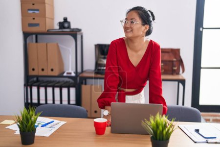 Photo for Young chinese woman business worker smiling confident standing by desk at office - Royalty Free Image