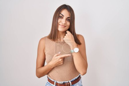 Téléchargez les photos : Jeune femme hispanique debout sur fond blanc à la hâte pointant pour regarder le temps, l'impatience, regardant la caméra avec une expression détendue - en image libre de droit
