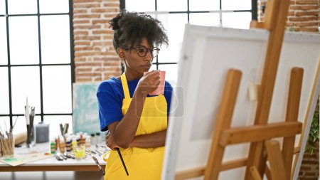 Téléchargez les photos : Artiste afro-américaine regardant dessiner tenant une tasse de café au studio d'art - en image libre de droit