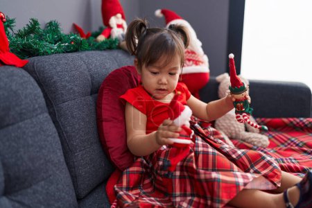 Foto de Adorable chica china sosteniendo juguetes de Navidad sentado en el sofá en casa - Imagen libre de derechos