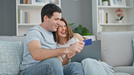 Foto de Hermosa pareja de compras con ordenador portátil y tarjeta de crédito sentado en el sofá sonriendo en casa - Imagen libre de derechos