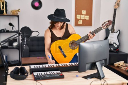 Photo for Middle age woman musician composing song playing classical guitar at music studio - Royalty Free Image