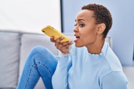 Foto de Mujer afroamericana hablando en smartphone sentada en sofá en casa - Imagen libre de derechos