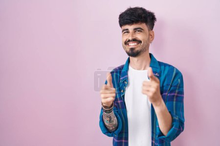 Photo for Young hispanic man with beard standing over pink background pointing fingers to camera with happy and funny face. good energy and vibes. - Royalty Free Image