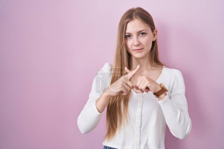 Téléchargez les photos : Jeune femme caucasienne debout sur fond rose expression de rejet croisant les doigts faisant signe négatif - en image libre de droit