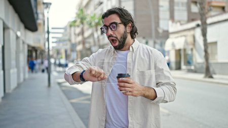 Téléchargez les photos : Jeune homme hispanique boire emporter café regarder surpris à la rue - en image libre de droit