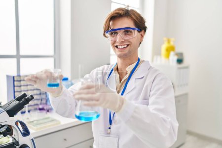 Téléchargez les photos : Jeune homme caucasien scientifique versant du liquide sur éprouvette au laboratoire - en image libre de droit