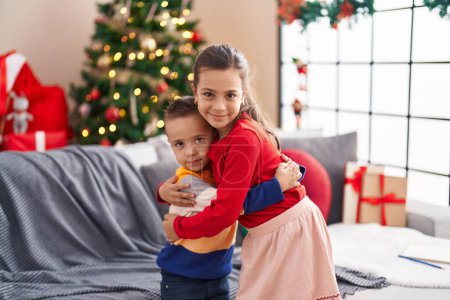 Foto de Hermano y hermana abrazándose de pie junto al árbol de Navidad en casa - Imagen libre de derechos