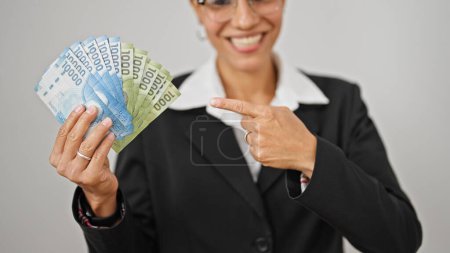 Foto de Joven hermosa mujer hispana trabajadora de negocios señalando pesos chilenos sonriendo sobre fondo blanco aislado - Imagen libre de derechos