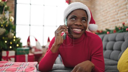 Téléchargez les photos : Femme afro-américaine parlant sur smartphone célébrant Noël à la maison - en image libre de droit