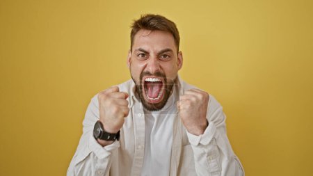 Wütender junger hispanischer Mann, gestresst und schreiend vor gelbem Hintergrund. Porträt eines wütenden Gesichtsausdrucks vor laufender Kamera.