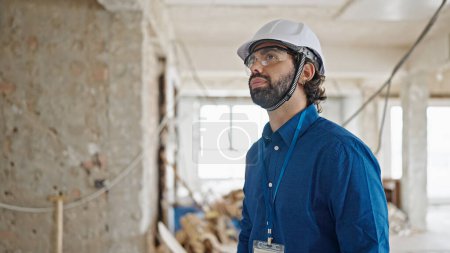 Téléchargez les photos : Jeune homme hispanique architecte debout avec un visage sérieux sur le chantier de construction - en image libre de droit