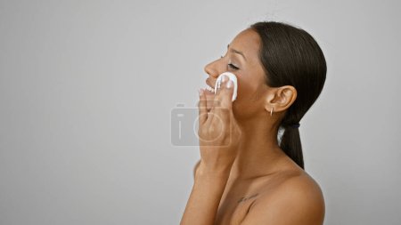 Téléchargez les photos : Jeune femme latine souriant visage de nettoyage confiant avec tampon de coton sur fond blanc isolé - en image libre de droit