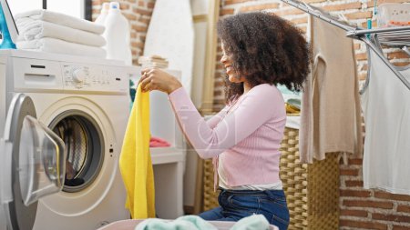 Foto de Mujer afroamericana lavando ropa sonriendo en la lavandería - Imagen libre de derechos
