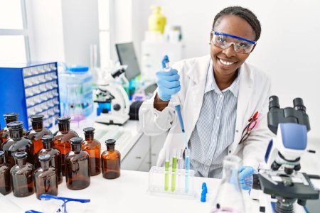 Foto de Científica afroamericana vertiendo líquido en tubo de ensayo en laboratorio - Imagen libre de derechos
