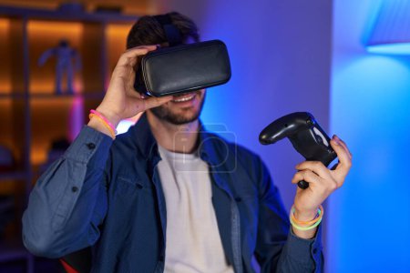 Téléchargez les photos : Jeune homme caucasien streamer jouer à un jeu vidéo en utilisant des lunettes de réalité virtuelle et joystick à la salle de jeu - en image libre de droit
