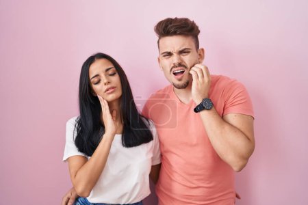 Photo for Young hispanic couple standing over pink background touching mouth with hand with painful expression because of toothache or dental illness on teeth. dentist concept. - Royalty Free Image