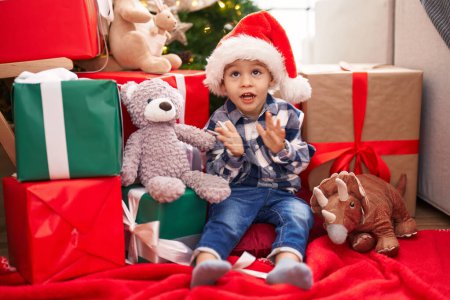 Photo for Adorable toddler sitting on floor by christmas gifts applauding at home - Royalty Free Image